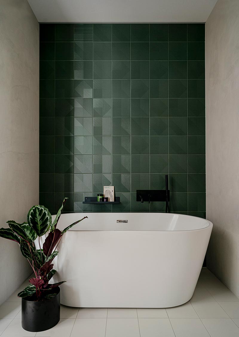 Voor de mooie badkamer zijn de betonstuc muren en vloer gecombineerd met een accentmuur bij het vrijstaand bad van groene geometrische tegels.