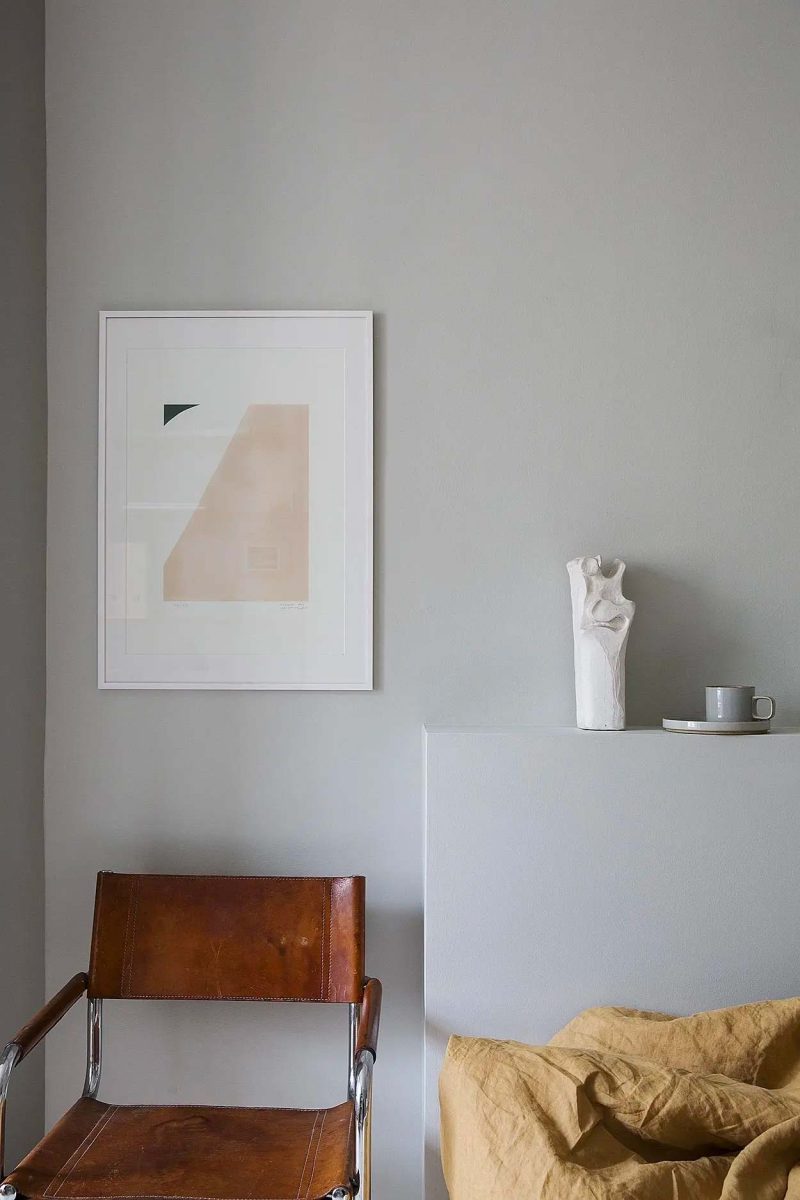 De cognac kleur stoel naast het bed is een hele stijlvolle toevoeging in deze slaapkamer met grijze muren.