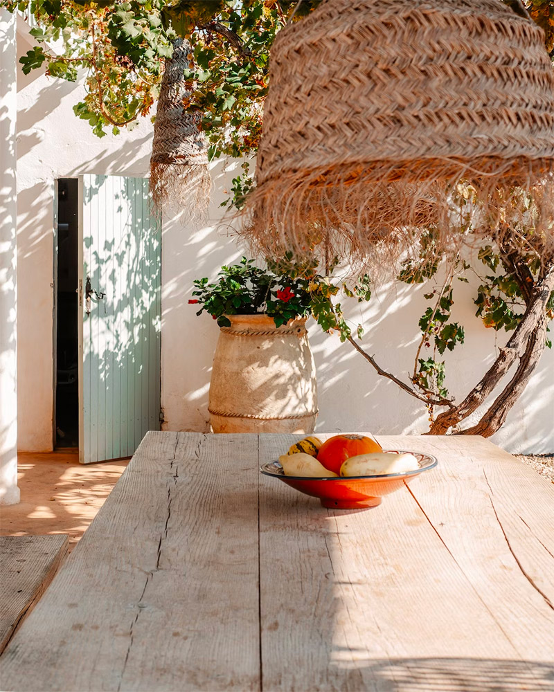 Een geweven hanglamp boven een rustieke houten eettafel geef je jouw tuin meteen dat fijne vakantiegevoel.