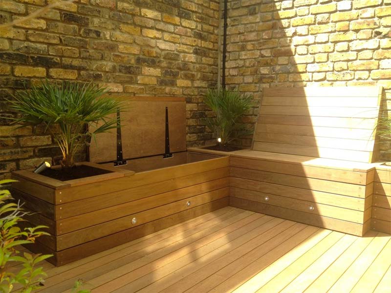 De op maat gemaakte houten bank in deze kleine tuin bevat niet alleen opbergruimte, maar ook leuke vaste plantenbakken.