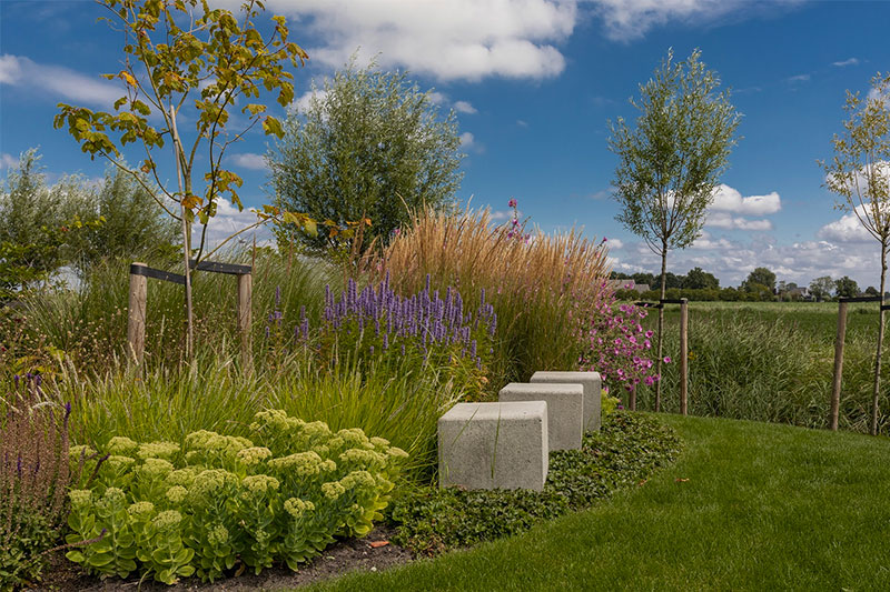 Van der Waal Tuinen koos in deze landelijke tuin voor grote bloembakken die mooi contrast staan met de ronde vormen van de borders en de weelderige beplanting. | Bron: Vanderwaaltuinen.nl