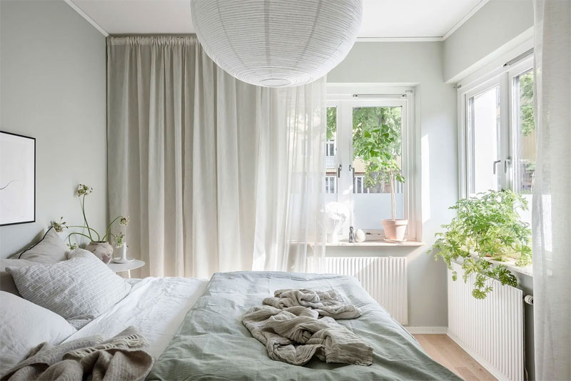 Lichte frisse slaapkamer, waar mintgroene muren gecombineerd zijn met een mintgroene bedsprei, witte gordijnen en een warme houten vloer.