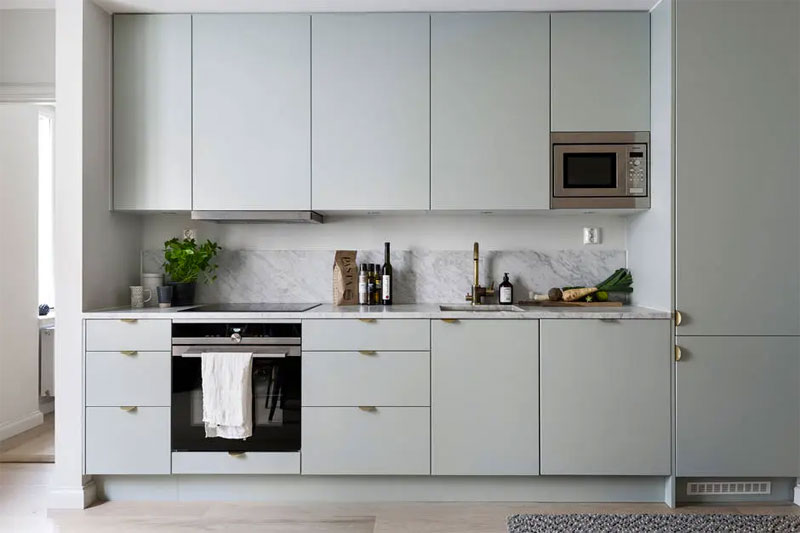 Moderne strakke mintgroene keuken met wit marmeren keukenblad en achterwand, en gouden deurgrepen.