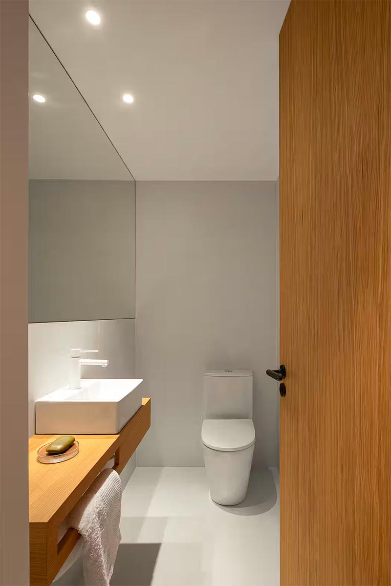 Strak minimalistisch toiletontwerp door David Olmos Arquitectos, waarbij beton ciré is gecombineerd met warm hout. De grote spiegel op maat voegt ook heel veel toe, zowel functioneel als esthetisch. | Fotografie: Ivo Tavares Studio