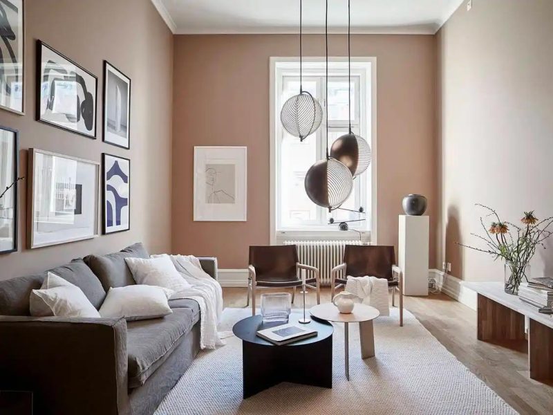 Hele mooie woonkamer met nude kleur muren gecombineerd met een houten vloer, licht vloerkleed en verschillende contrasterende zwarte accenten.