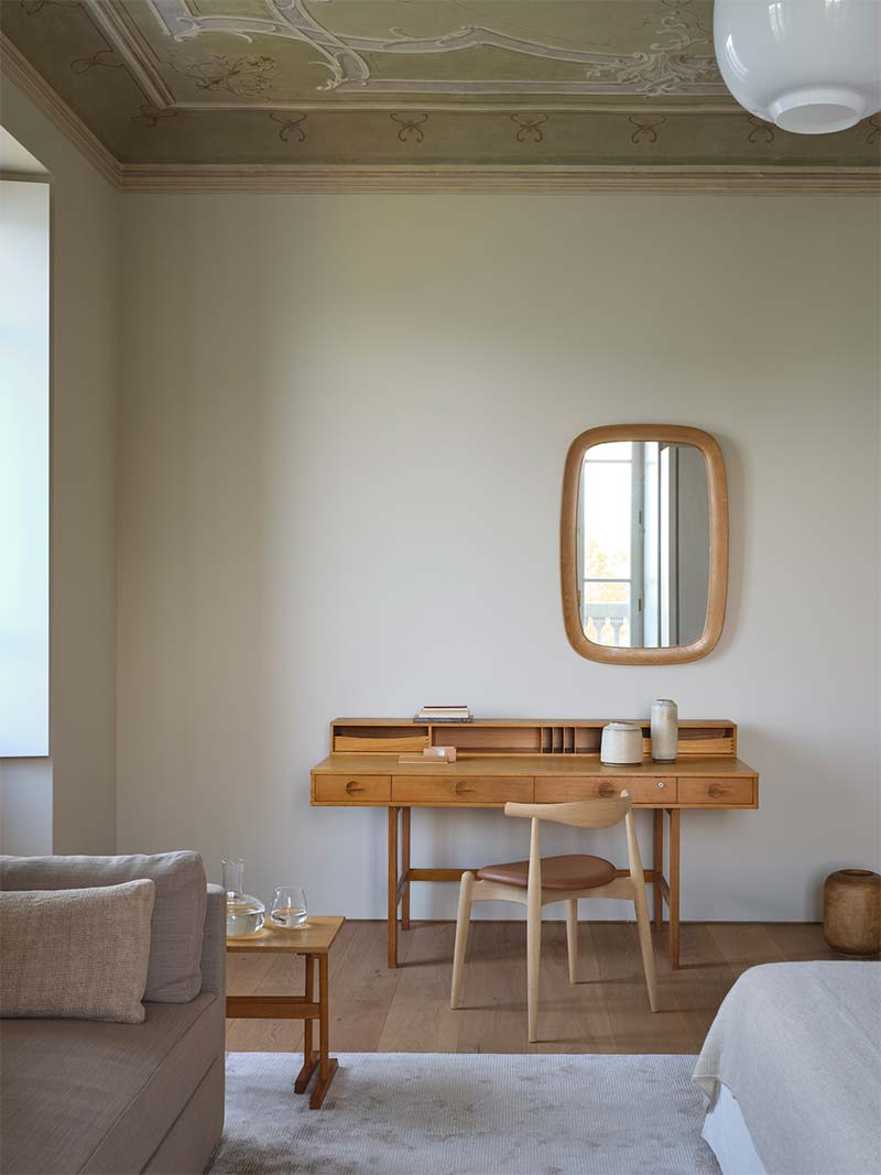 Deze slaapkamer is voorzien van een verzameling vintage Deense stukken, zoals de wandspiegel uit de jaren 30, bijzettafels uit de jaren 60 en het Flip Flop-dressoir, vergezeld van de Carl Hansen & Son CH20 Elbow-stoel.