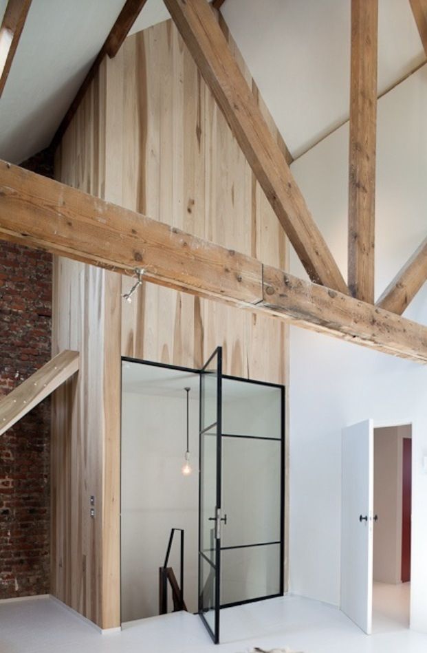 De stalen deur met glas staat super stoer bij de houten wandbekleding en de houten balken aan het plafond in deze woonkamer.