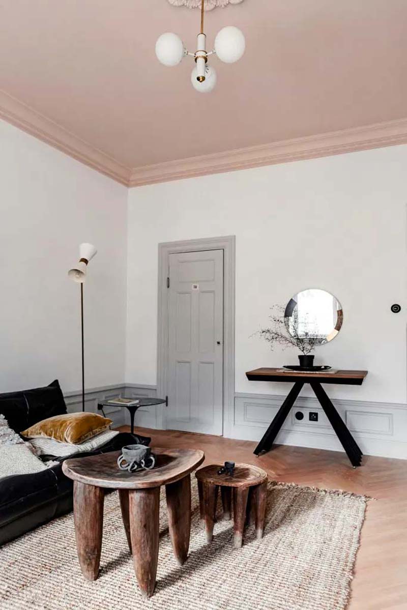 Mooie karakteristieke woonkamer met roze plafond, witte muren, lichtgrijze deur, jute vloerkleed en boomstam tafeltjes