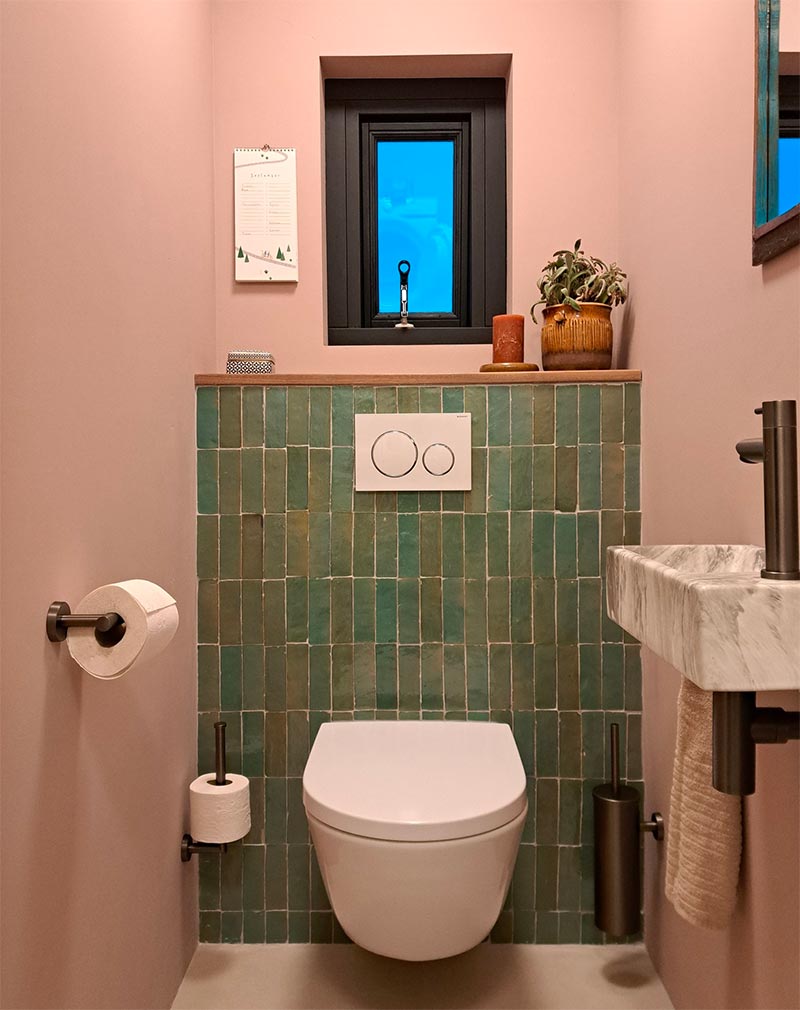 In dit leuke toilet zijn de Bejmat Vert Gris tegels van Designtegels.nl gecombineerd met oud roze wanden, zwarte en witte accenten, en een wit marmeren fonteintje.