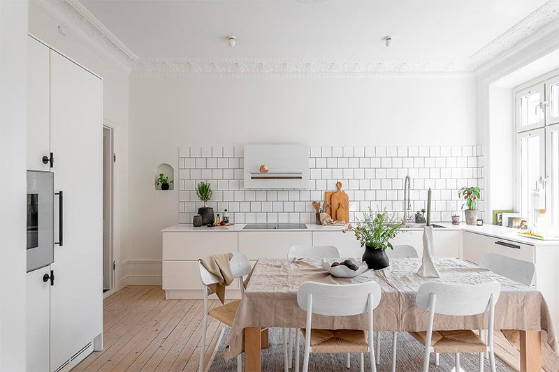 Een hele fijne lichte keuken in Scandinavische stijl, met strakke witte kasten en gezellige houten eettafel.