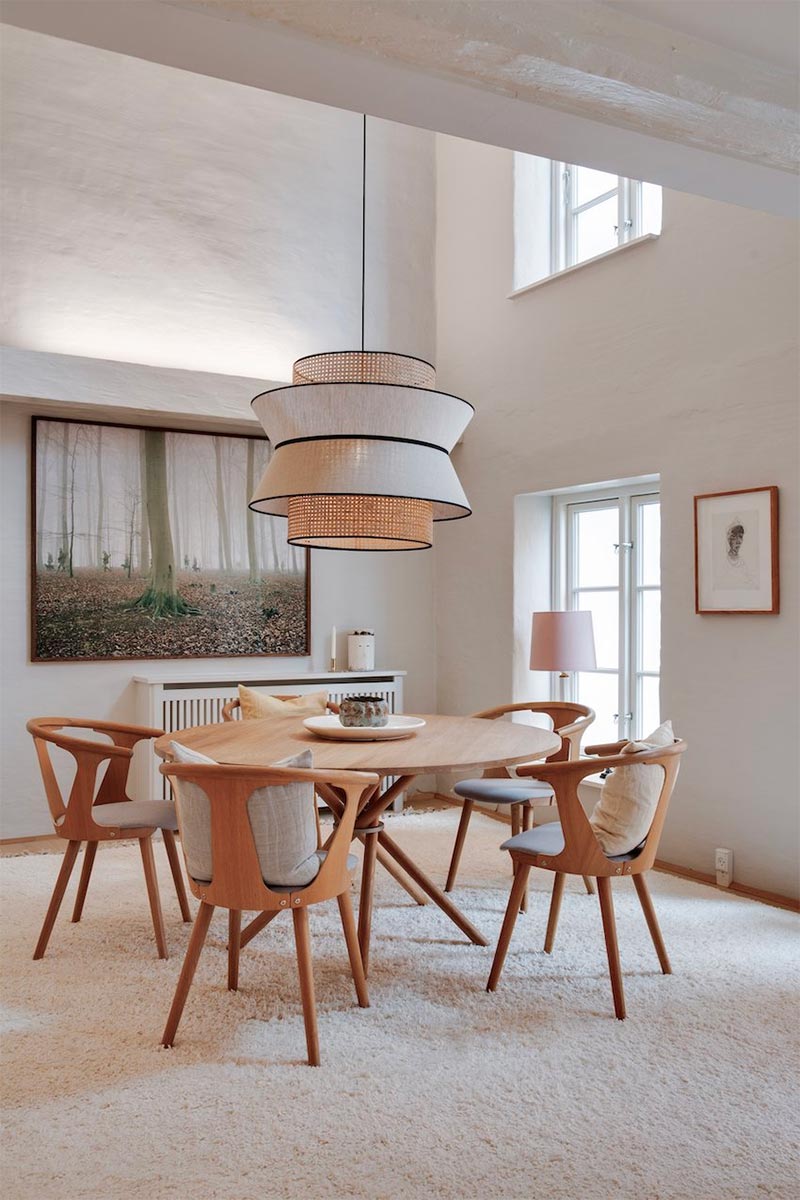 De grote hanglamp vormt de blikvanger boven de houten ronde eettafel en eetkamerstoelen.