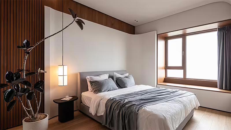 In de master bedroom is een groot sculpturaal wit hoofdbord gecreëerd met afgeronde hoeken. Het hoofdbord vormt een mooi contrast met de houten vloer en de teakhouten wandbekleding.
