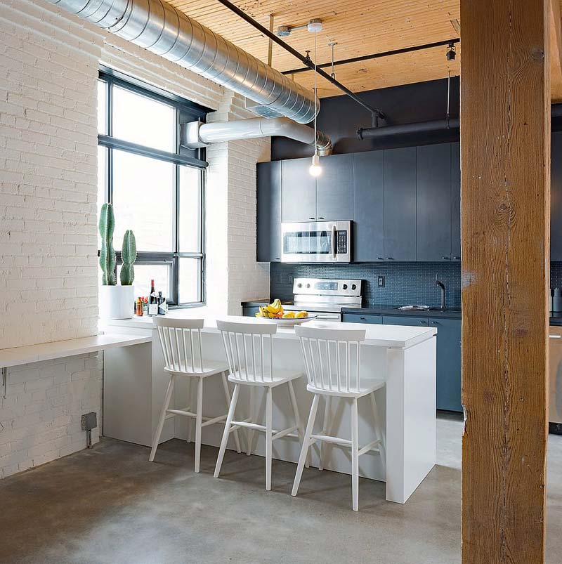 In dit kleine loft appartement is gekozen voor een open schiereiland keuken met drie mooie bijpassende witte barkrukken.