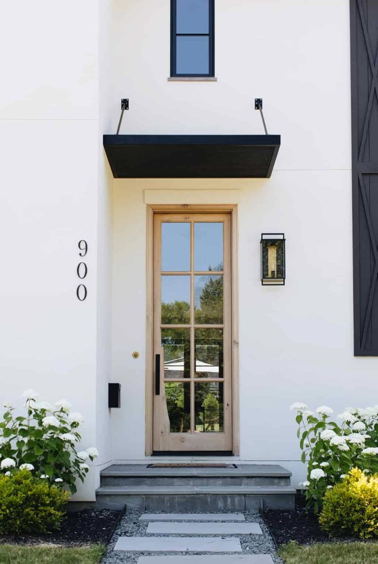 De strakke zwarte deurluifel past pefect bij de zwarte kozijnen en raamluiken van dit prachtige witte huis.