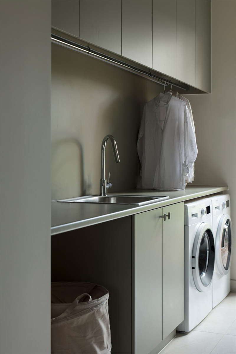 Op maat gemaakte wasruimte met een olijfgroene wasmachine kast met twee wasmachines naast elkaar.