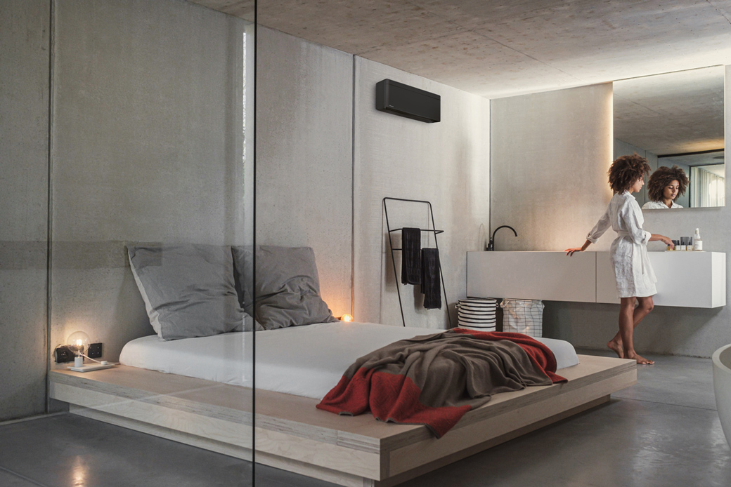 In deze stoere slaapkamer met betonstuc is er gekozen een bijpassende zwarte airco aan de wand.